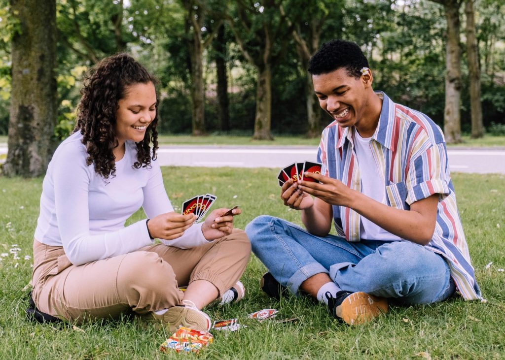 A joyful moment of two friends playing cards on the grass in a park, enjoying leisure time together.